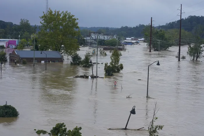 Asheville flood | Castle Insurance Wide view of a flooded town with water covering streets, submerged streetlights, trees, and partially submerged buildings in the background.